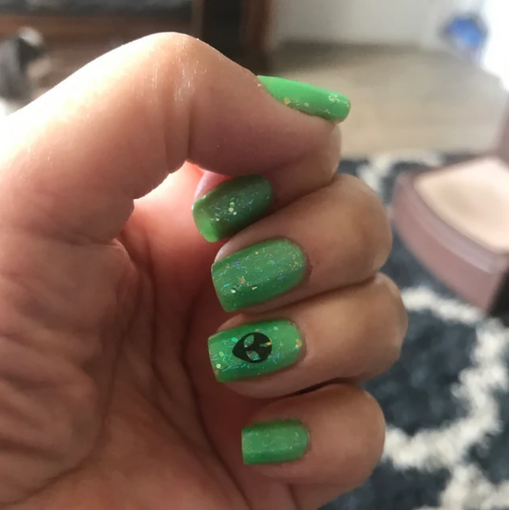 Glittery bright green nail polish with a black alien nail decal on the ring finger