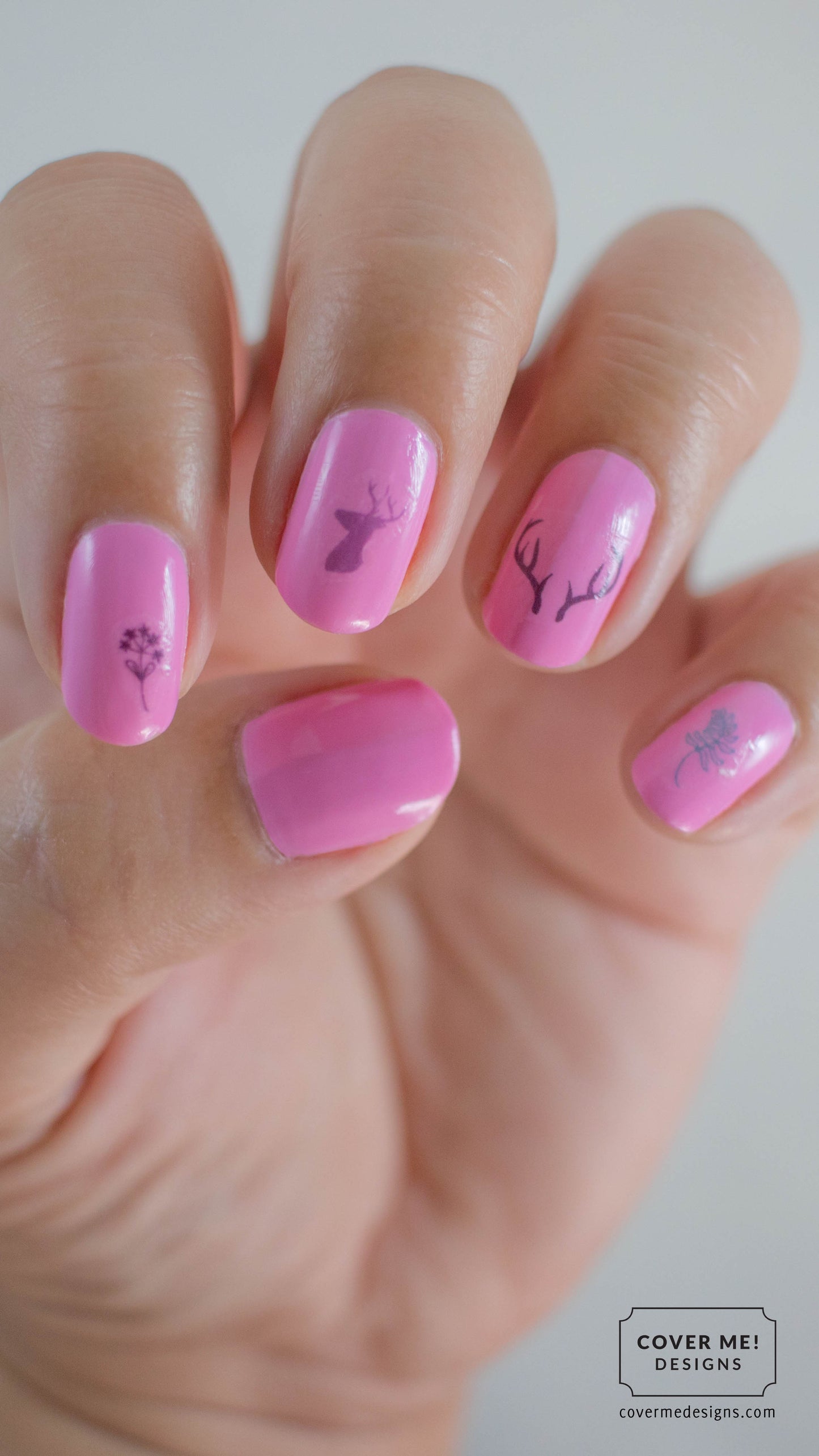 Pink nail polish with nail stickers of deer, antlers, and plants