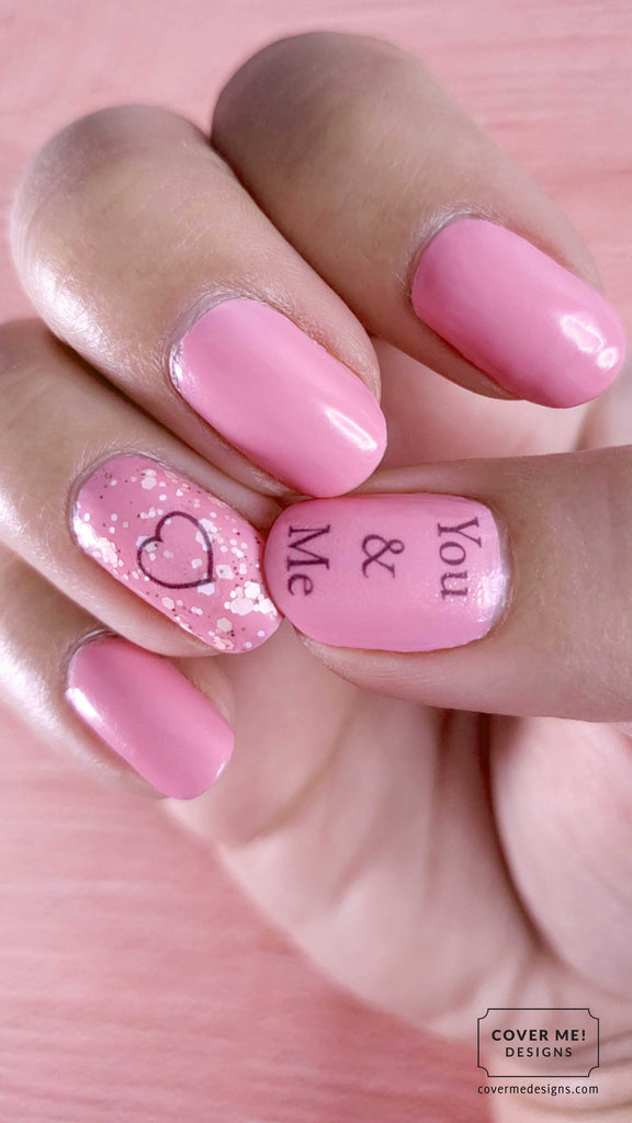 Pink nail art for a wedding with the text "you and me" and a heart over glitter nail polish